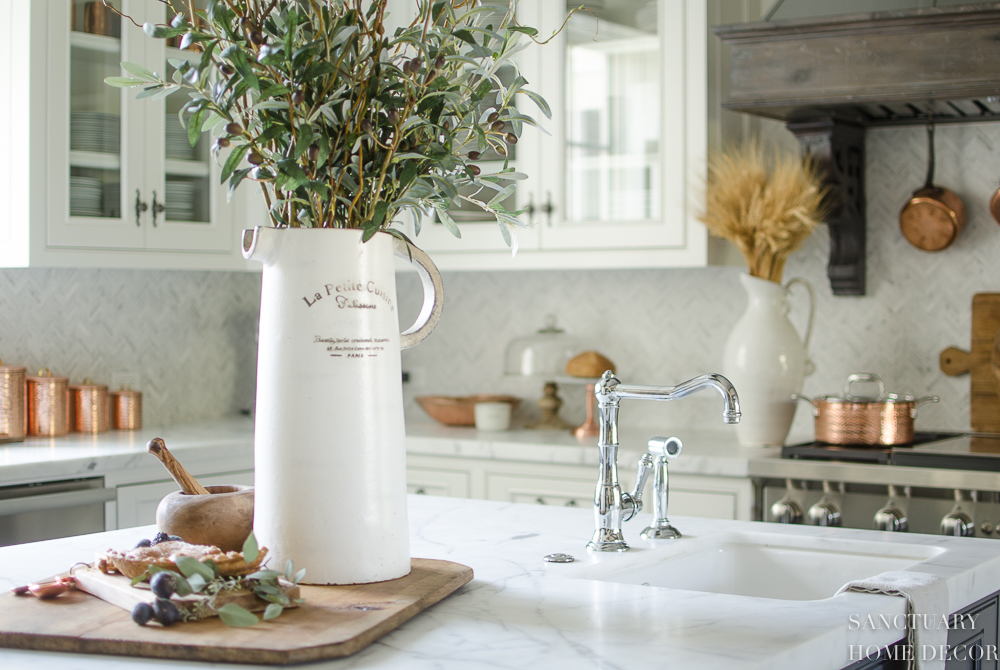 5 Minute Fall Decorating Tips-White country kitchen with pendant lights and glass front cabinets. White marble countertops.