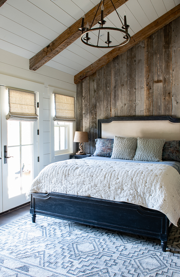 Reclaimed wood accent wall in bedroom with chandelier and Smith and Noble Roman Shades