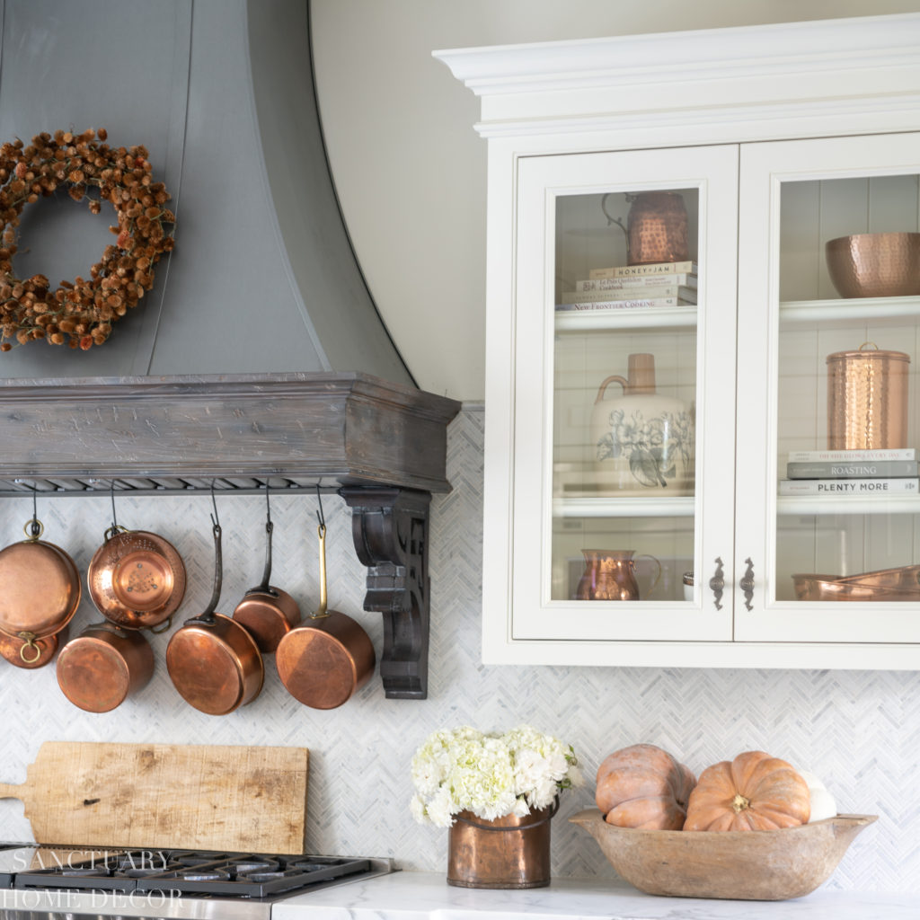 Farmhouse kitchen with fall decorating. Glass front cabinets with copper accents. Range hood with wreath. Copper pots