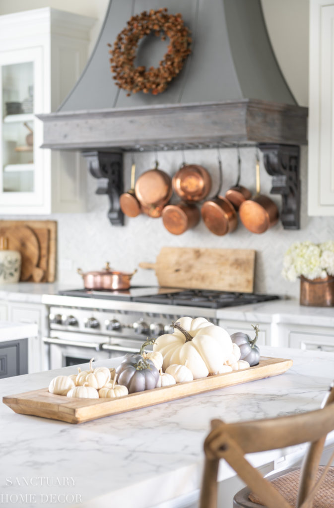 Farmhouse kitchen with fall decorating. Glass front cabinets with copper accents. Range hood with wreath. Copper pots. Faux pumpkins